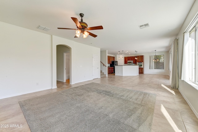 unfurnished living room with arched walkways, ceiling fan, visible vents, and baseboards