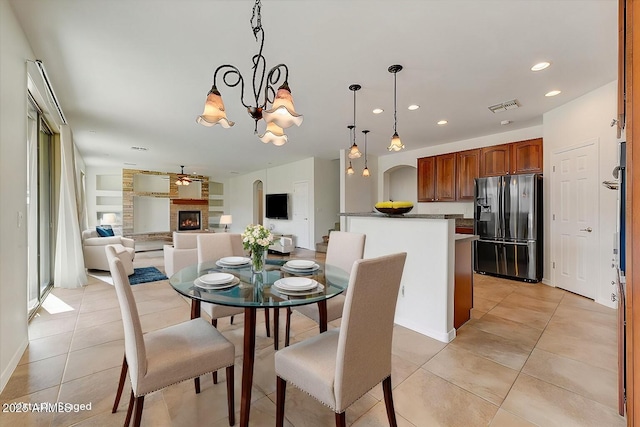 dining space featuring a warm lit fireplace, visible vents, ceiling fan with notable chandelier, light tile patterned flooring, and recessed lighting