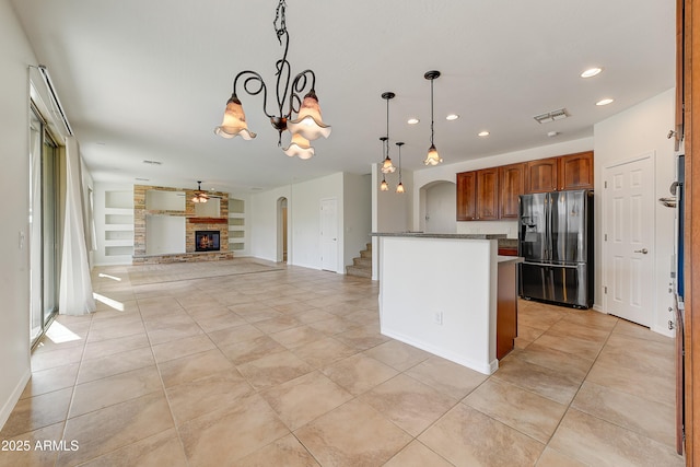 kitchen with arched walkways, light tile patterned floors, stainless steel fridge with ice dispenser, a glass covered fireplace, and decorative light fixtures