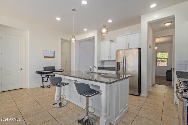 kitchen with dark stone counters, a center island with sink, sink, white cabinets, and appliances with stainless steel finishes