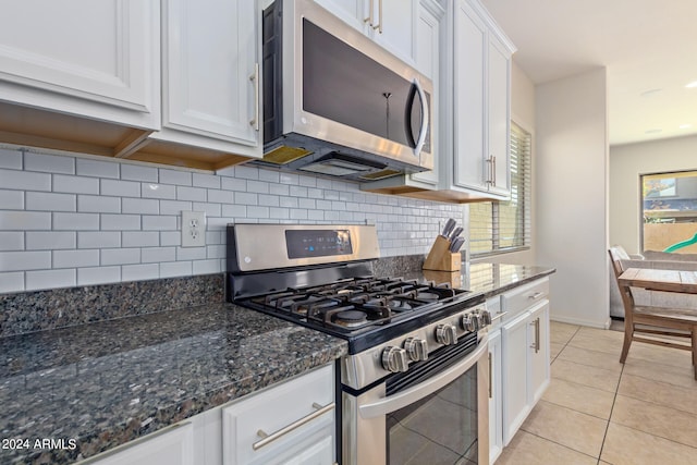 kitchen with decorative backsplash, stainless steel appliances, dark stone countertops, light tile patterned floors, and white cabinetry