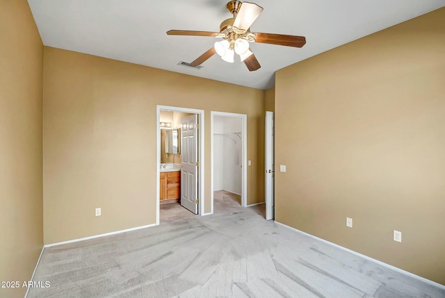 unfurnished bedroom with connected bathroom, a walk in closet, light colored carpet, ceiling fan, and a closet