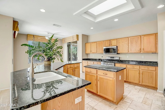 kitchen featuring sink, light brown cabinets, dark stone counters, an island with sink, and stainless steel appliances