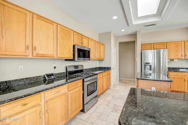 kitchen with dark stone countertops, stainless steel appliances, a center island, and light brown cabinets