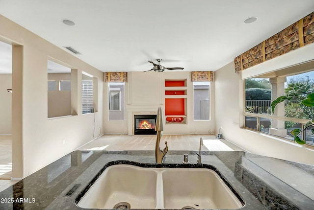 kitchen featuring ceiling fan, sink, and dark stone countertops