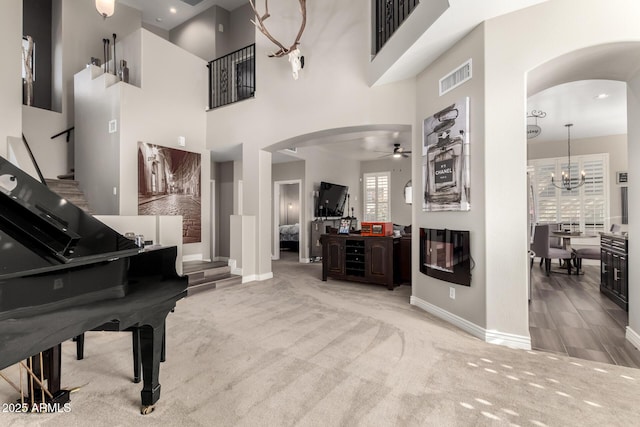 misc room with ceiling fan with notable chandelier, carpet, and a high ceiling