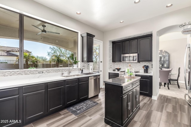 kitchen featuring sink, appliances with stainless steel finishes, a kitchen island, ceiling fan, and backsplash