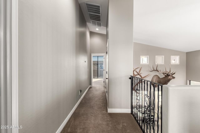 hallway with dark colored carpet and lofted ceiling