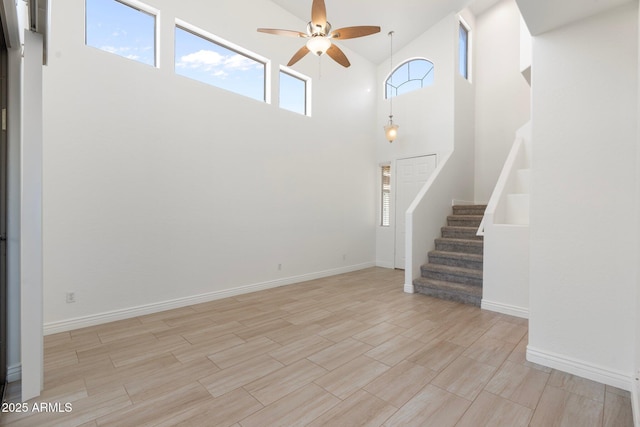 unfurnished living room featuring ceiling fan and a towering ceiling