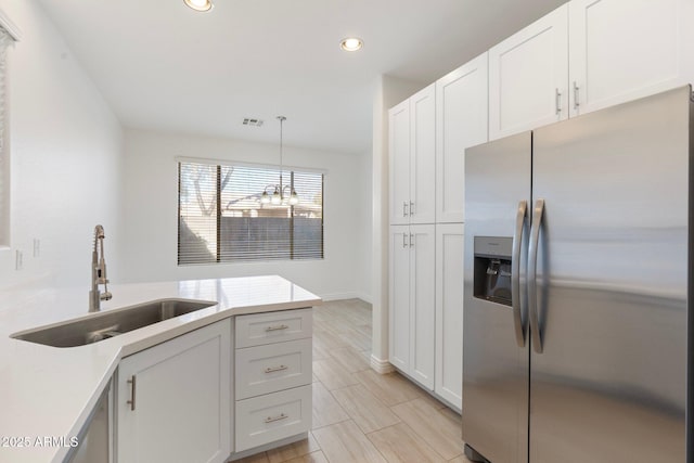 kitchen featuring sink, white cabinetry, stainless steel fridge, and hanging light fixtures