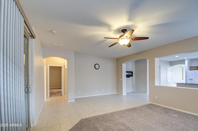 unfurnished room featuring visible vents, light carpet, a ceiling fan, arched walkways, and light tile patterned floors