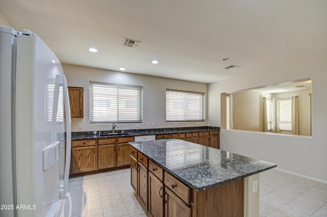 kitchen with visible vents, a kitchen island, brown cabinets, white fridge with ice dispenser, and a sink