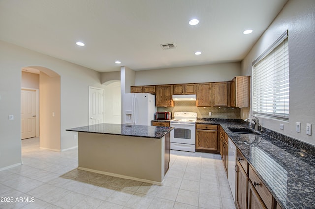 kitchen with white appliances, visible vents, arched walkways, a sink, and under cabinet range hood