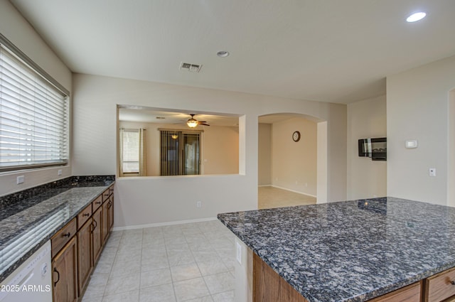 kitchen with dark stone countertops, visible vents, arched walkways, white dishwasher, and brown cabinets