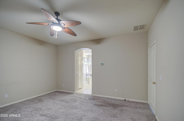 spare room with visible vents, baseboards, light carpet, arched walkways, and a ceiling fan