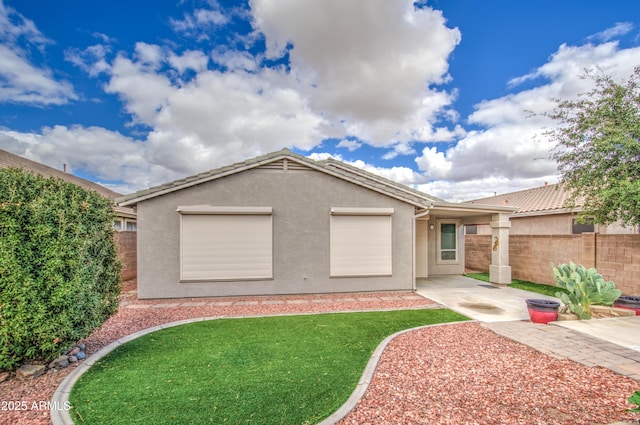 rear view of house with a tiled roof, stucco siding, a yard, and fence