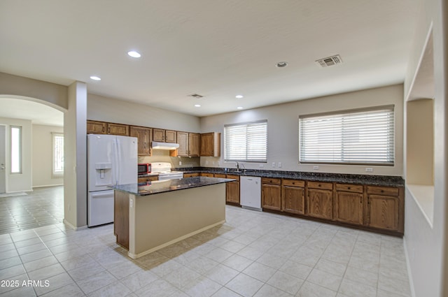 kitchen with visible vents, a kitchen island, under cabinet range hood, arched walkways, and white appliances