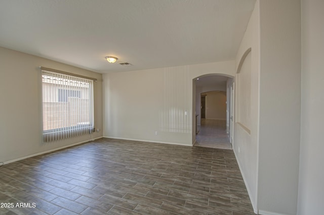 spare room with arched walkways, visible vents, baseboards, and dark wood-style floors