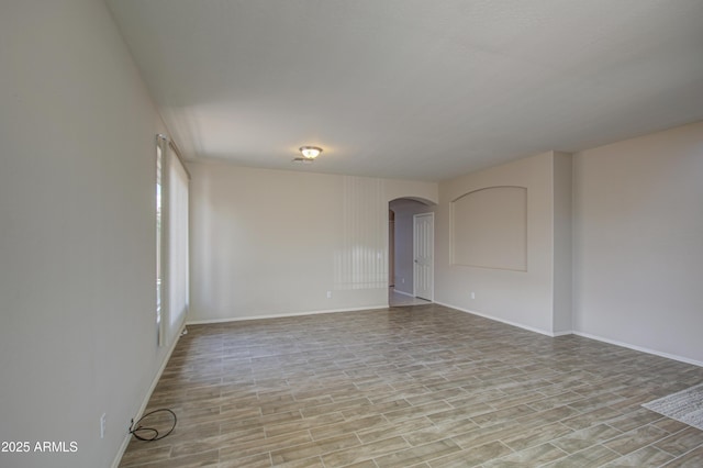 spare room featuring light wood-type flooring, arched walkways, and baseboards