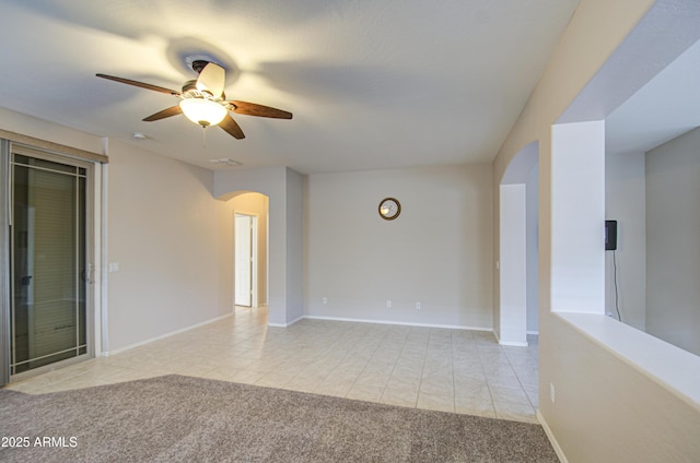 empty room featuring light tile patterned floors, baseboards, arched walkways, ceiling fan, and light colored carpet