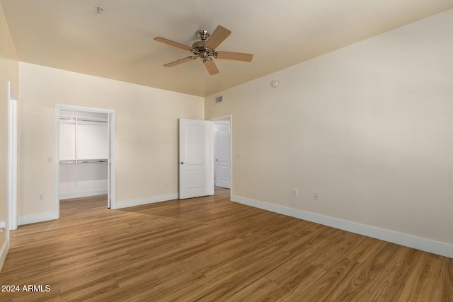 unfurnished bedroom featuring ceiling fan, hardwood / wood-style floors, a closet, and a walk in closet