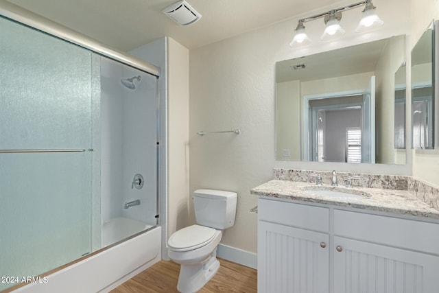 full bathroom featuring hardwood / wood-style floors, enclosed tub / shower combo, vanity, and toilet