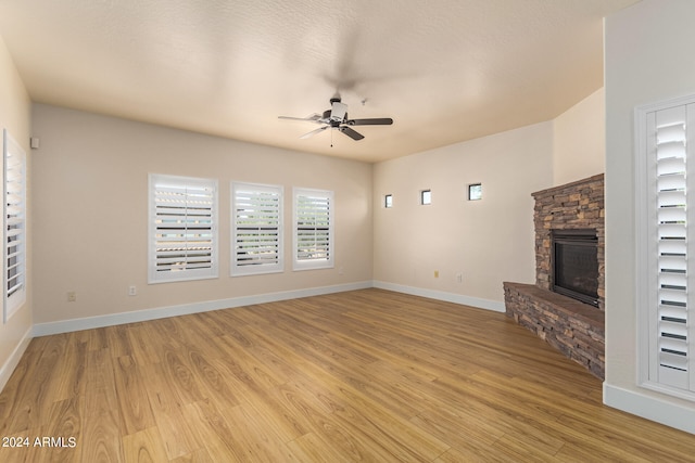 unfurnished living room featuring ceiling fan, light hardwood / wood-style flooring, and a stone fireplace