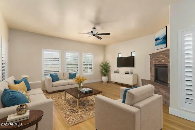 living room featuring ceiling fan, a stone fireplace, and light wood-type flooring