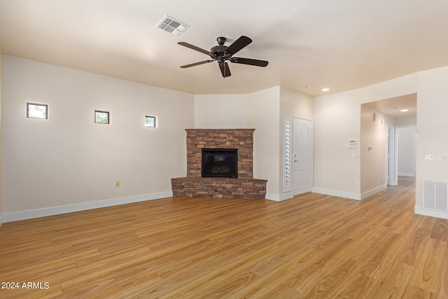 unfurnished living room featuring light hardwood / wood-style floors, ceiling fan, and a stone fireplace