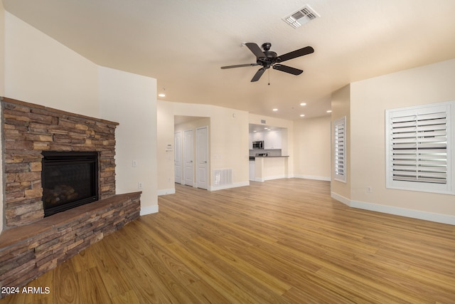 unfurnished living room with ceiling fan, light wood-type flooring, and a stone fireplace