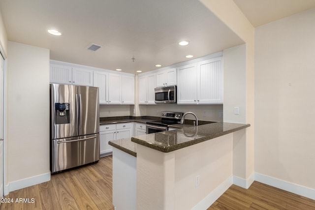 kitchen featuring white cabinets, appliances with stainless steel finishes, kitchen peninsula, and dark stone countertops