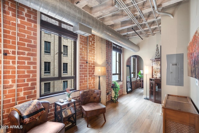 living area with hardwood / wood-style flooring, brick wall, and electric panel