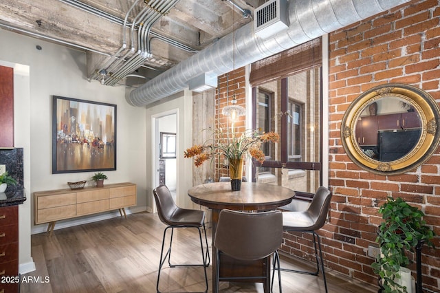 dining space featuring brick wall and wood-type flooring