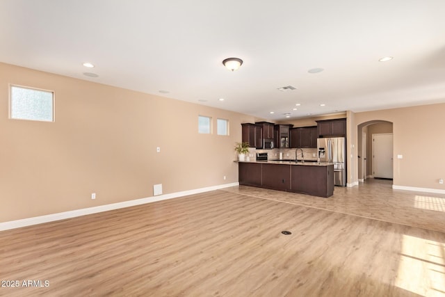 3443 E Jasper Dr, Gilbert, AZ 85296 - unfurnished living room featuring arched walkways, baseboards, light wood-style flooring, recessed lighting, and a sink