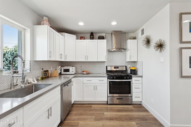 2129 W Indianola Ave, Phoenix, AZ 85015 - kitchen featuring wall chimney range hood, stainless steel appliances, a sink, decorative backsplash, and light wood-style flooring