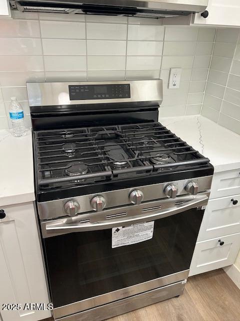 interior details with gas stove, decorative backsplash, light countertops, white cabinets, and light wood-style floors