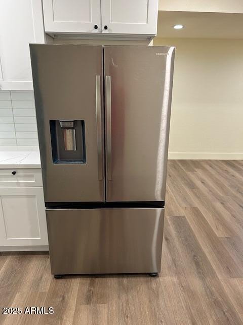 room details with light wood-style flooring, light stone countertops, white cabinetry, and stainless steel fridge with ice dispenser