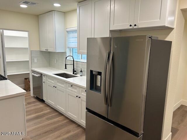 kitchen with visible vents, a sink, appliances with stainless steel finishes, white cabinetry, and light wood-type flooring