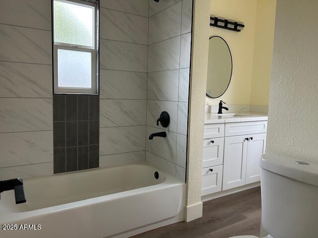 bathroom featuring tub / shower combination, toilet, wood finished floors, a textured wall, and vanity