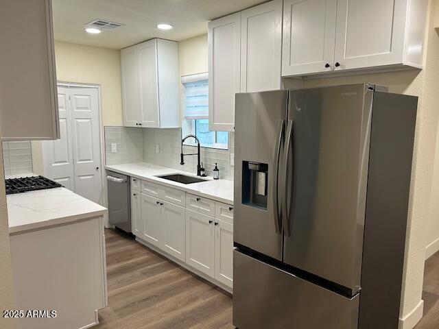 kitchen with a sink, white cabinetry, appliances with stainless steel finishes, light wood finished floors, and decorative backsplash