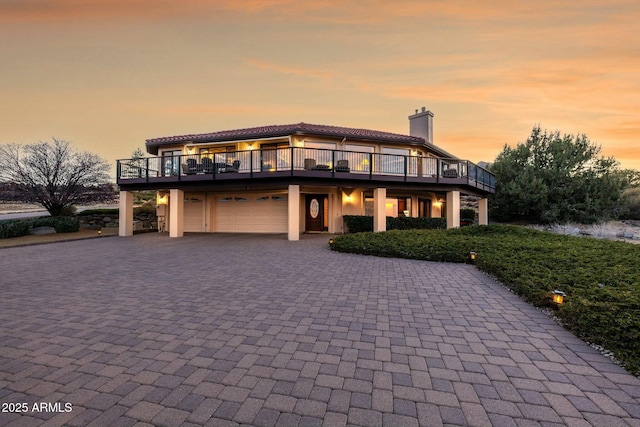 view of front of house featuring stucco siding, an attached garage, a chimney, and decorative driveway