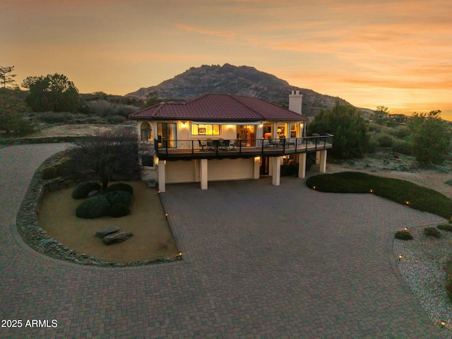 view of front of house featuring a chimney, a garage, a tiled roof, decorative driveway, and a mountain view