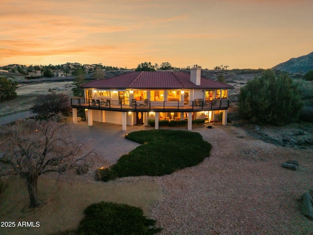 back of property at dusk featuring a tile roof, driveway, a chimney, and a patio