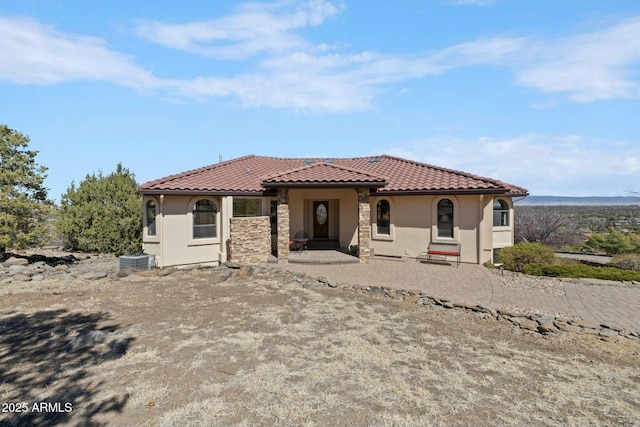 view of front facade featuring a tiled roof, cooling unit, stone siding, and stucco siding