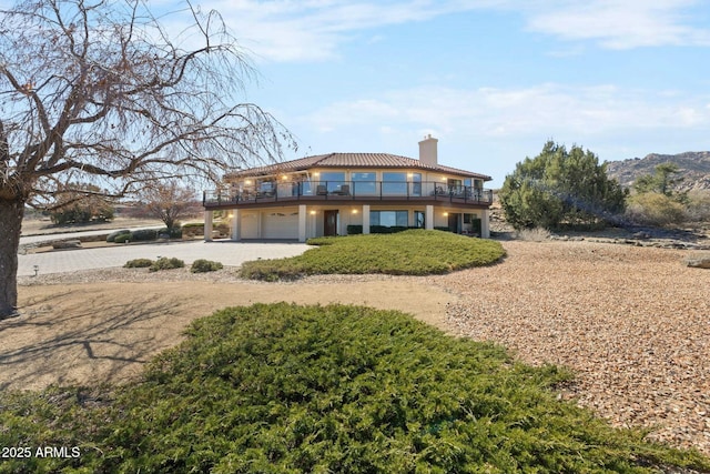 view of front of property featuring a garage, driveway, a balcony, and a chimney