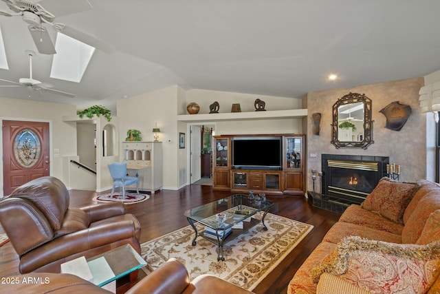 living room with a premium fireplace, vaulted ceiling with skylight, ceiling fan, and wood finished floors