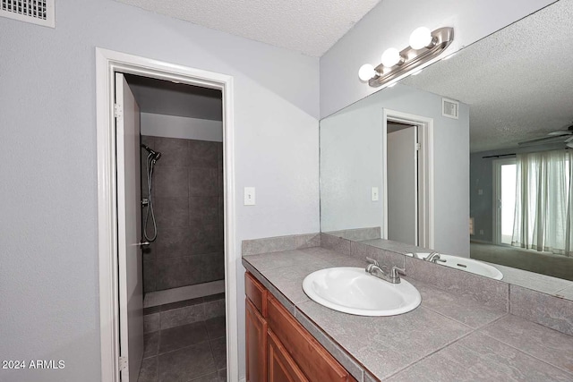 bathroom with a textured ceiling, vanity, ceiling fan, tiled shower, and tile patterned flooring