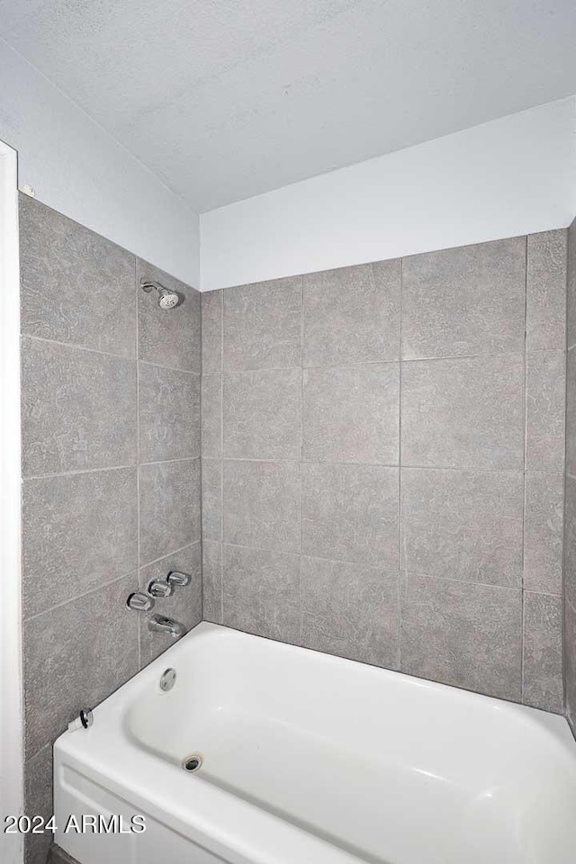 bathroom with a textured ceiling and tiled shower / bath combo