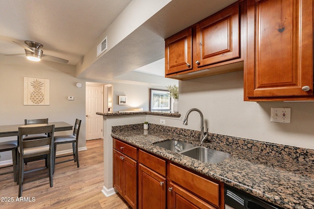 kitchen featuring visible vents, light wood-style flooring, a sink, dark stone counters, and ceiling fan