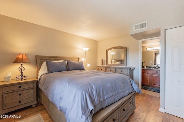 bedroom with light wood-style flooring, visible vents, and ensuite bathroom